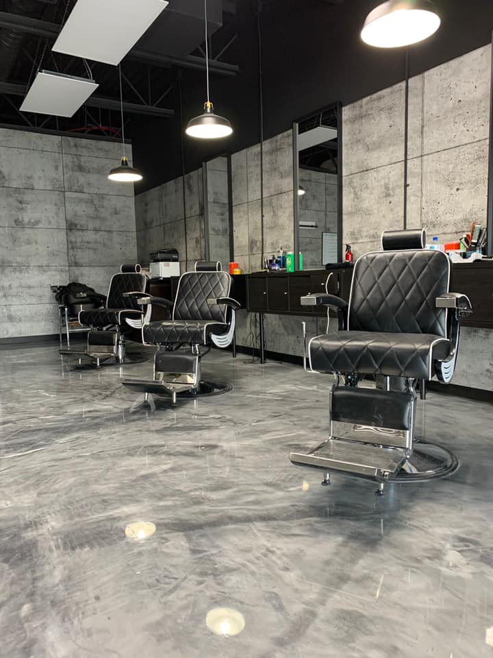 Luxury barbershop interior with concrete walls, pendant lights, and quilted black barber chairs